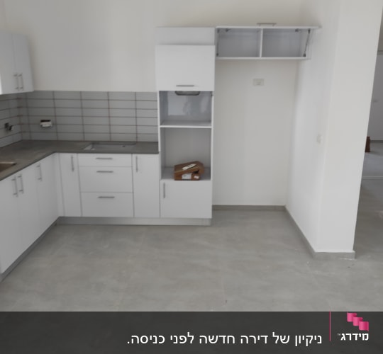 מטבח ריק עם ארונות לבנים ורצפה נקייה